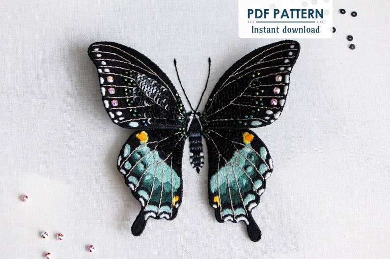 The finished 3D butterfly made from thread painting embroidery and beading, on a white fabric background with a few beads/sequins scattered in the corners and the "PDF Pattern Instant Download" sticker in the right hand corner.