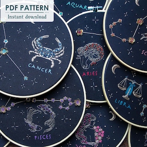 May include: A set of 10 embroidery hoops with different zodiac signs, including Aries, Cancer, Libra, Pisces, Scorpio, and Aquarius. Each hoop features a black background with white and gold embroidery, and the name of the zodiac sign is written below the design.