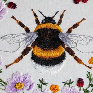 Another close up of the embroidered bumble bee and flowers, with the bee centered in the image and flowers showing on left, right, and bottom on a white fabric ground. Note, this is a pdf pattern.