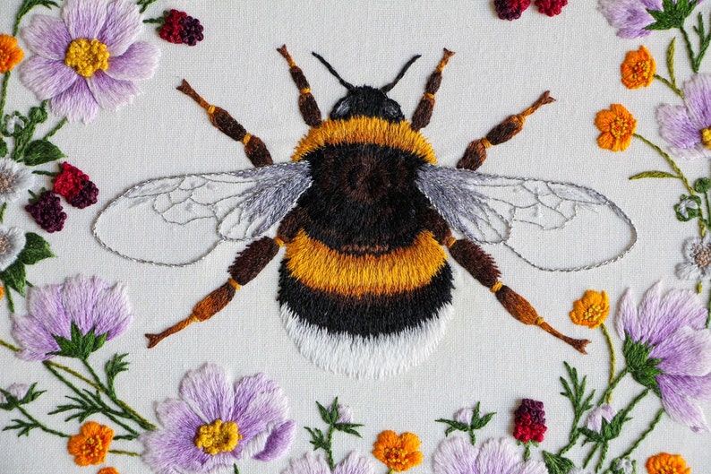 Another close up of the embroidered bumble bee and flowers, with the bee centered in the image and flowers showing on left, right, and bottom on a white fabric ground. Note, this is a pdf pattern.