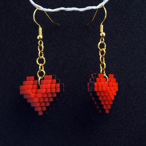 Könnte beinhalten: Ein Paar Ohrringe mit goldenen Ketten und roten und schwarzen pixelartigen Herzanhängern.