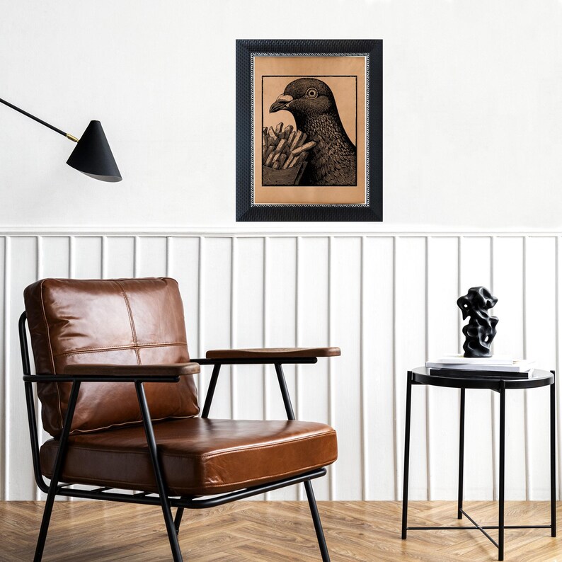 May include: Black framed art print featuring a detailed illustration of a pigeon holding a container of french fries. The artwork is set against a tan background and is mounted on a white wall. The print is a unique piece of wall decor.