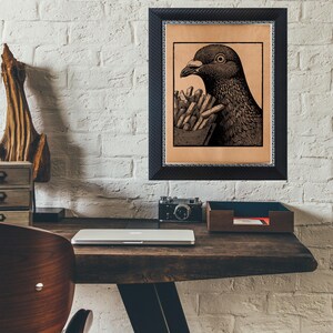 May include: Black framed art print featuring a detailed illustration of a pigeon holding a carton of french fries. The artwork is set against a tan background and is mounted on a white brick wall.