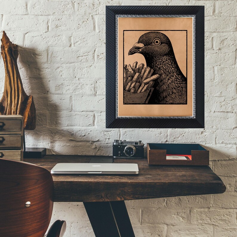 May include: Black framed art print featuring a detailed illustration of a pigeon holding a carton of french fries. The artwork is set against a tan background and is mounted on a white brick wall.