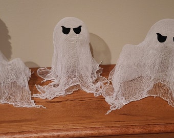 May include: Three white ghost decorations with black eye cutouts. The ghosts are made of a gauzy material and are arranged in a row. These Halloween decorations are perfect for adding a spooky touch to any home.