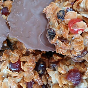 May include: Close-up of a crispy, golden brown treat with a variety of toppings, including dried fruit, nuts, and chocolate. The treat is a popular dessert or snack.