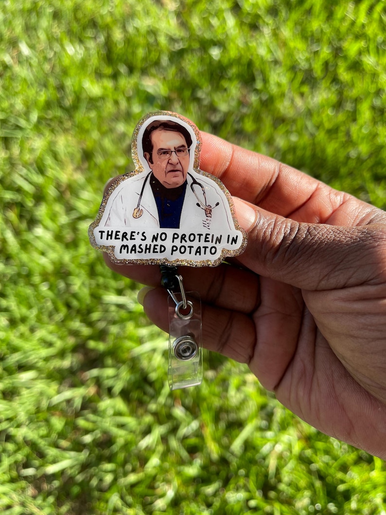 May include: A badge reel featuring a glittery gold border and an illustration of a doctor wearing a white coat and stethoscope. The text below the figure reads, "THERE'S NO PROTEIN IN MASHED POTATO" in black capital letters on a white background.