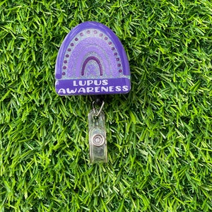 May include: Purple glitter rainbow with the text "Lupus Awareness" on a retractable badge reel.