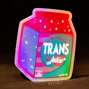 May include: A holographic sticker in the shape of a milk carton with the words "TRANS Juice" in a circular design. The carton is pink, red, and blue with a heart and the text "60 Calories" and "4.2 fl oz".