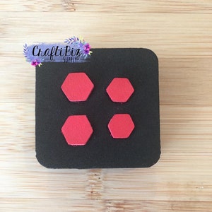 May include: A black square with four red hexagon shapes. The shapes are arranged in two rows of two. The text "CraftiBiz SUPPLY" is in the upper left corner.