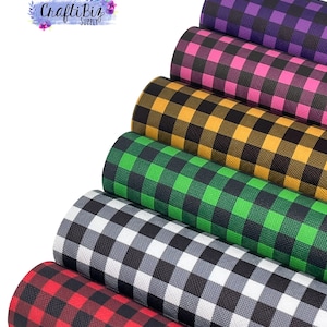 Puede incluir: Varios rollos de tela con estampado de cuadros de búfalo en diferentes colores. Los colores incluyen rojo, negro, blanco, verde, amarillo, rosa y morado. El logotipo de CraftiBiz Supply es visible.