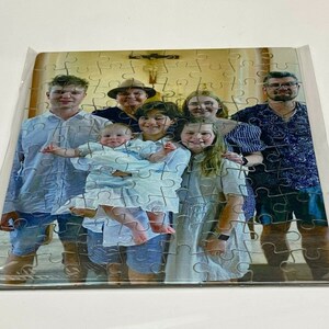 Puede incluir: Un rompecabezas de retrato familiar con un grupo de siete personas, incluyendo un beb&eacute;, de pie frente a una iglesia. Las piezas del rompecabezas son visibles en la imagen.
