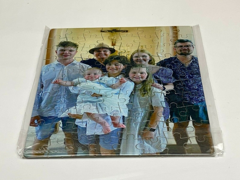 Puede incluir: Un rompecabezas de retrato familiar con un grupo de siete personas, incluyendo un beb&eacute;, de pie frente a una iglesia. Las piezas del rompecabezas son visibles en la imagen.