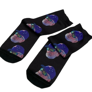 May include: A pair of black socks with a repeating pattern of a man wearing a blue cap with the Australian flag and sunglasses. The man has a white beard and is looking forward.