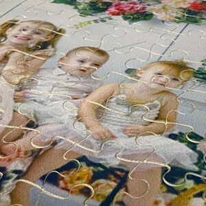 Puede incluir: Un rompecabezas con una foto de tres ni&ntilde;os. Los ni&ntilde;os llevan vestidos blancos y sonr&iacute;en. Las piezas del rompecabezas son visibles alrededor de los bordes de la foto.