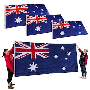 May include: Three Australian flags of different sizes, with the largest flag being held by two people. The flags are blue with a red cross and white stars.
