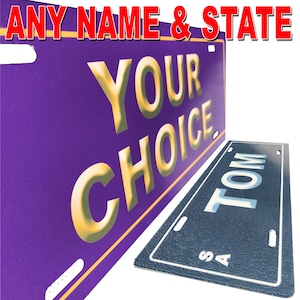 Puede incluir: Dos placas de matrícula de color morado y azul con texto blanco. La placa morada dice "YOUR CHOICE" en letras doradas. La placa azul dice "TOM" en letras blancas con "SA" debajo.