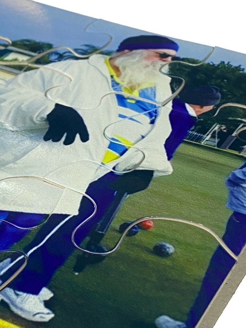 Puede incluir: Un grupo de personas jugando a los bolos sobre un campo de hierba verde. La persona en primer plano lleva una chaqueta blanca, una camisa azul y amarilla, guantes negros y un turbante azul. La persona sostiene un palo de bolos blanco.