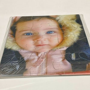 Puede incluir: Primer plano de un beb&eacute; que lleva una chaqueta rosa y blanca con capucha de piel. El beb&eacute; tiene ojos azules y mira a la c&aacute;mara.