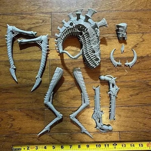 Peut inclure: Ensemble de pièces grises imprimées en 3D représentant un extraterrestre, comprenant une tête, des jambes et d'autres éléments. Les pièces sont disposées sur une surface en bois, suggérant un kit de modélisme.