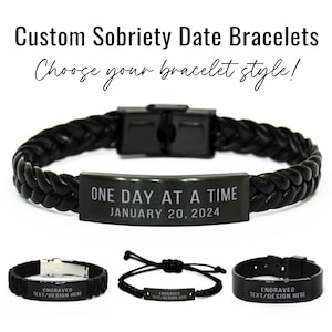 May include: Three black leather bracelets with engraved metal plates. The top bracelet has the text "ONE DAY AT A TIME JANUARY 20, 2024". The bottom two bracelets have the text "ENGRAVED TEXT/DESIGN HERE".