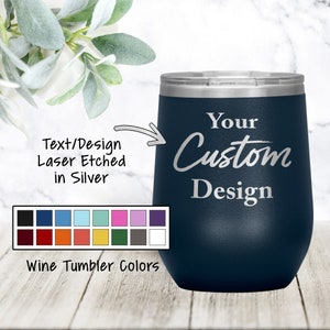 以下が含まれることがあります： 「Your Custom Design」と銀色のレーザー彫刻が施されたネイビーブルーのステンレス製ワインタンブラー。タンブラーは白い大理石の表面に置かれています。タンブラーの下には、タンブラーの色を18色から選べるカラーチャートが表示されています。
