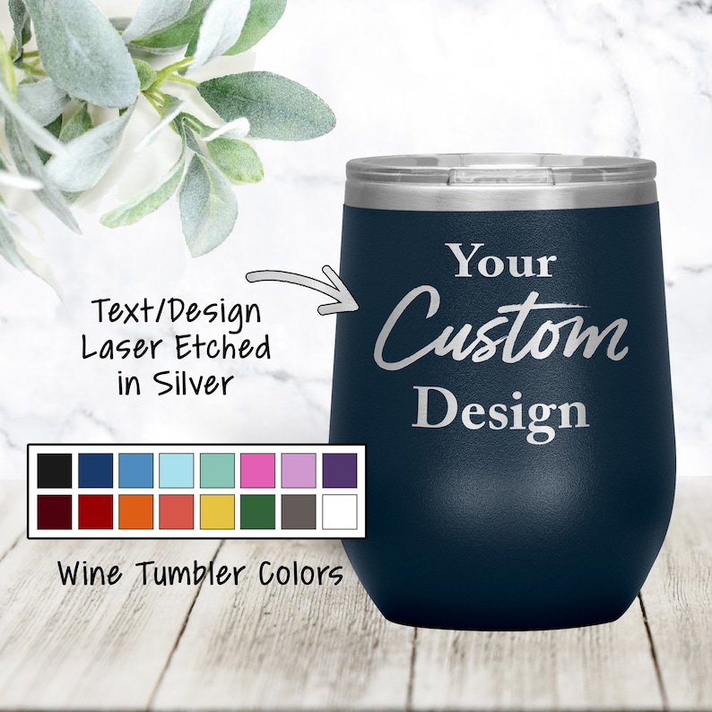 以下が含まれることがあります： 「Your Custom Design」と銀色のレーザー彫刻が施されたネイビーブルーのステンレス製ワインタンブラー。タンブラーは白い大理石の表面に置かれています。タンブラーの下には、タンブラーの色を18色から選べるカラーチャートが表示されています。