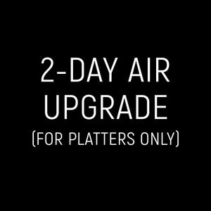 May include: Black background with white text that reads "2-DAY AIR UPGRADE (FOR PLATTERS ONLY)". The text is centered and in a sans-serif font.
