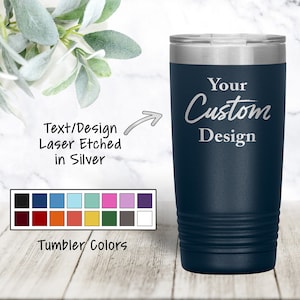May include: A navy blue stainless steel tumbler with a silver lid. The tumbler has a custom design that says "Your Custom Design" in silver lettering. The tumbler is shown on a wooden surface with a color chart of different tumbler colors.