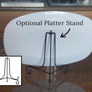 May include: White oval platter with an optional black metal stand. The stand has three legs with a decorative scroll design. The text "Optional Platter Stand" is written above the stand.