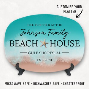 May include: A turquoise and beige oval platter with a beach scene and the text "Life is better at the Johnson Family Beach House - Gulf Shores, AL - Est. 2023".