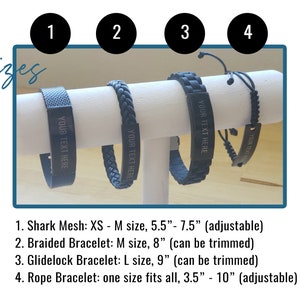 May include: Four different styles of black bracelets with adjustable sizing. The bracelets are displayed on a white stand. The bracelets have a silver plate with the text "YOUR TEXT HERE" engraved on them.  The bracelets are numbered 1 through 4.