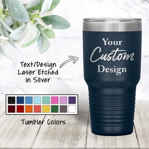 May include: Navy blue insulated tumbler with a silver lid. The tumbler has the words "Your Custom Design" etched in silver. The image also shows a color chart with various tumbler color options.