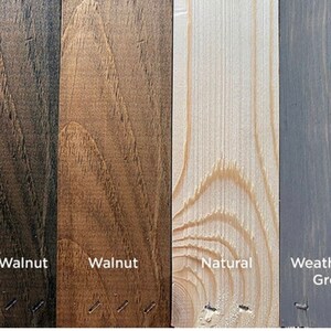 May include: A collection of four wood stain samples: Dark Walnut, Walnut, Natural, and Weathered Grey. Each sample is a vertical plank with visible wood grain and the stain name printed below. The samples are arranged side by side.