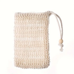 May include: A beige, woven soap bag with a drawstring closure. The rectangular bag has a textured surface and a loop for hanging. A small wooden bead is attached to the drawstring.