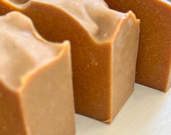 May include: Close-up of several bars of handmade soap. The soap is light brown with a slightly textured surface. The bars are rectangular with a wavy top, suggesting a natural, artisanal product.