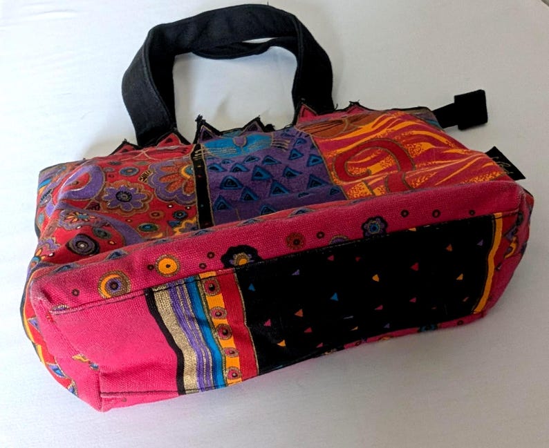 Puede incluir: Un bolso tipo tote con dise&ntilde;o de patchwork que presenta paneles de tela en colores rojo, morado, naranja y negro vibrantes. El bolso incluye asas negras, una base negra con peque&ntilde;os tri&aacute;ngulos coloridos y varios patrones florales y geom&eacute;tricos.