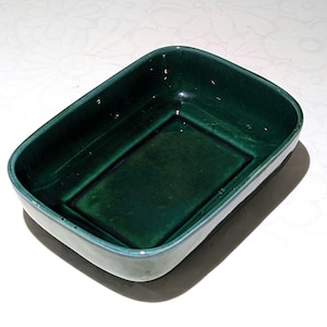 May include: A rectangular, emerald green ceramic baking dish. The dish has a glossy finish and a slightly raised rim. The interior features a recessed rectangular base. The dish is suitable for baking and serving.
