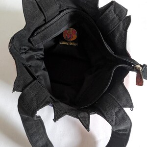 Puede incluir: Un bolso de tela negro con un borde superior en forma de estrella y dos asas. El interior est&aacute; forrado con tela negra y cuenta con un bolsillo con cremallera con un parche de logotipo circular y multicolor que contiene el texto "Cloud 9" en cursiva.