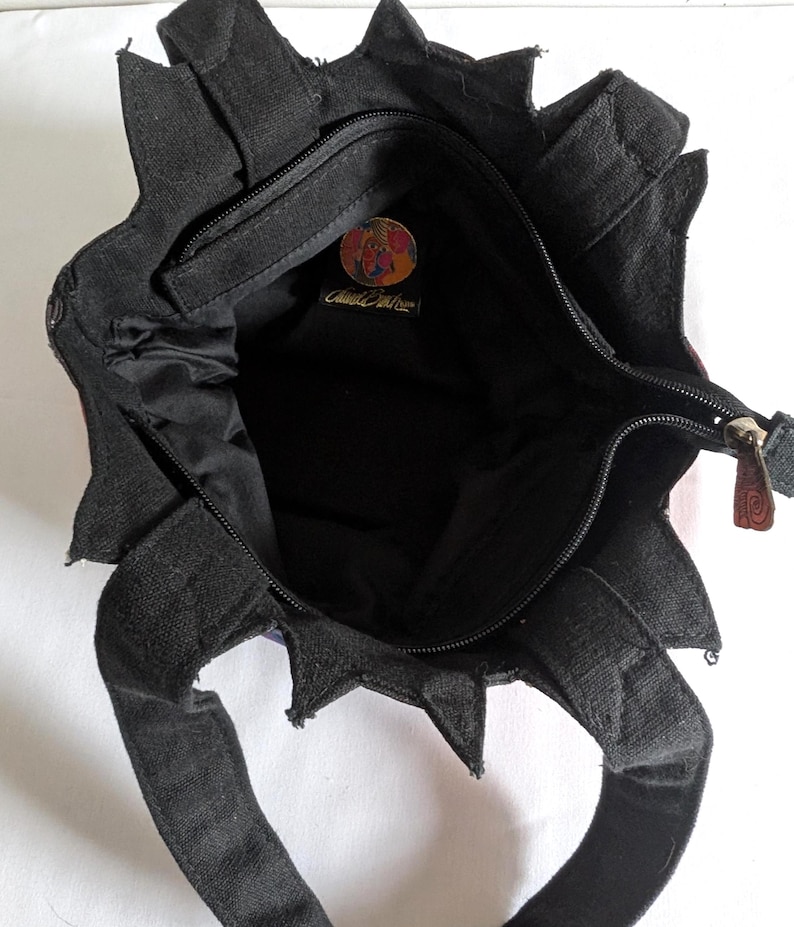Puede incluir: Un bolso de tela negro con un borde superior en forma de estrella y dos asas. El interior est&aacute; forrado con tela negra y cuenta con un bolsillo con cremallera con un parche de logotipo circular y multicolor que contiene el texto "Cloud 9" en cursiva.