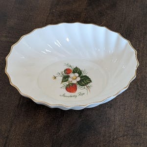 Peut inclure: Bol en céramique blanc avec un bord festonné et une bordure dorée. Le bol présente un motif de fraise au centre avec les mots "Strawberry Ripe". Le bol a un design cannelé et est parfait pour servir des fruits ou des salades.