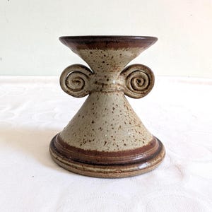 Peut inclure: Un bougeoir en céramique mouchetée avec un dessus et une base évasés, avec deux accents décoratifs en spirale. Le bougeoir a un bord et une base marron, avec un corps beige et marron.