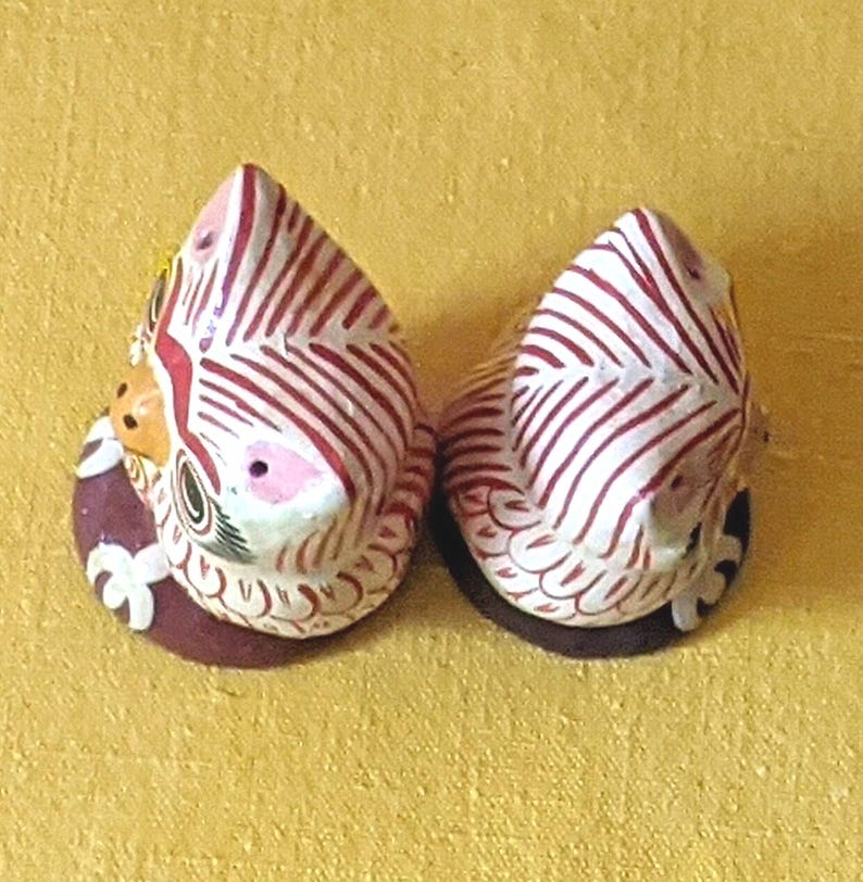 May include: Two small, hand-painted ceramic figurines shaped like birds, featuring white bodies with intricate red striped patterns, yellow beaks, and dark brown circular bases. The figurines are viewed from above, showing detailed painted feathers.
