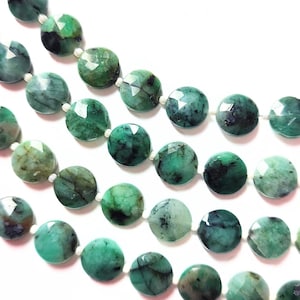 Puede incluir: Una hebra de cuentas de piedras preciosas de color verde esmeralda, cada cuenta está facetada y tiene una forma redonda. Las cuentas están enhebradas en un hilo blanco.