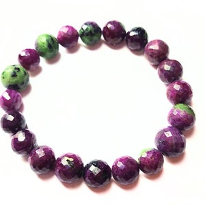 Puede incluir: Un brazalete hecho de piedras preciosas facetadas verdes y moradas. El brazalete está hecho de 18 cuentas.