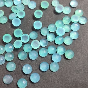 May include: A collection of round, faceted gemstones in shades of light blue and teal. The gemstones are scattered across a dark surface, showcasing their polished, translucent appearance. These gemstones are suitable for jewelry making.