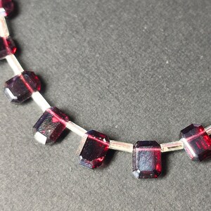 May include: A necklace made of dark red gemstone beads strung on a silver chain. The beads are rectangular and faceted.