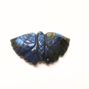 May include: A carved labradorite gemstone in the shape of a butterfly. The gemstone is a deep blue with iridescent flashes of color.