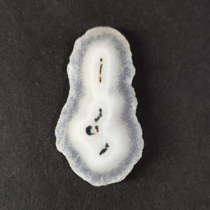 Puede incluir: Una rebanada de ágata blanca con un patrón azul oscuro y marrón. El ágata es translúcida y tiene una superficie lisa y pulida.