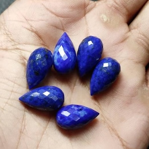 May include: Six teardrop-shaped lapis lazuli gemstones in various shades of blue. The gemstones are faceted and have a polished finish.